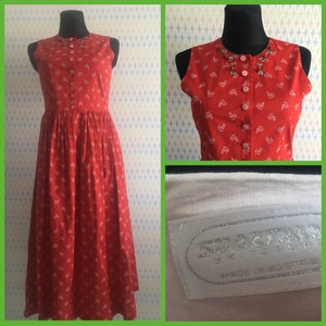 Könnte beinhalten: Ein rotes, ärmelloses Kleid mit weißem Blumenmuster und Knopfleiste. Das Kleid hat einen weißen Kragen mit Perlenbesatz und ein weißes Etikett mit der Aufschrift "Sportmax" und "Made in Austria".