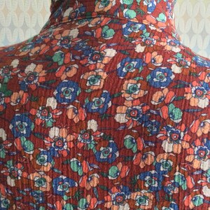 Pu&ograve; includere: Un tessuto rosso con un motivo floreale. I fiori sono in tonalit&agrave; di blu, arancione e bianco. Il tessuto ha una superficie testurizzata.