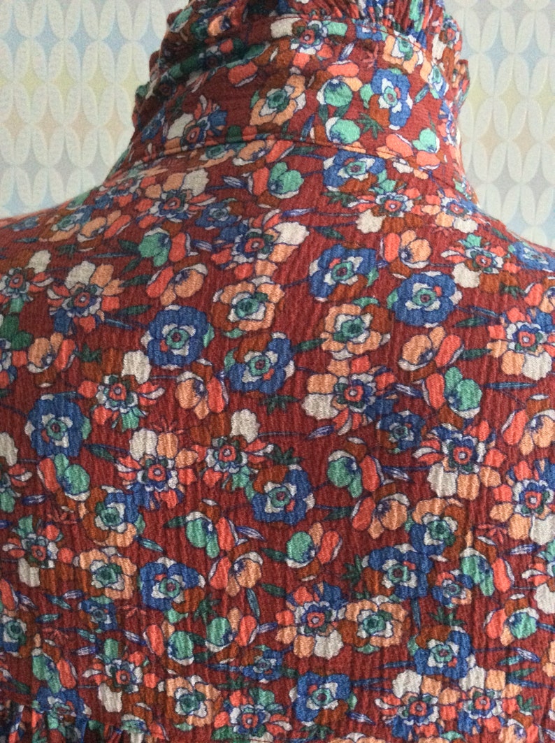 Pu&ograve; includere: Un tessuto rosso con un motivo floreale. I fiori sono in tonalit&agrave; di blu, arancione e bianco. Il tessuto ha una superficie testurizzata.