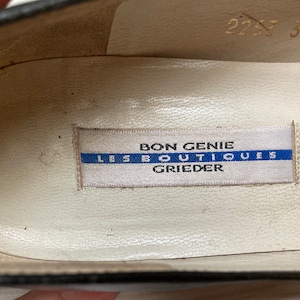 May include: Close-up of the inside of a black shoe with a white label that reads "Bon Genie Les Boutiques Grieder".
