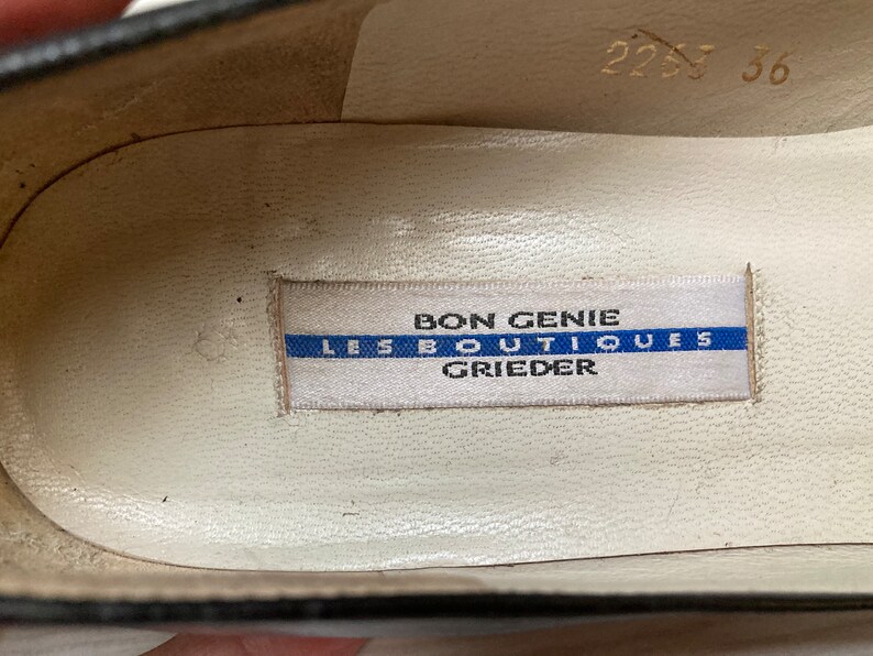 May include: Close-up of the inside of a black shoe with a white label that reads "Bon Genie Les Boutiques Grieder".