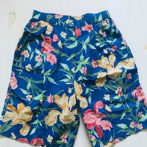 Pode incluir: Shorts azuis com estampa floral, cintura alta e bolsos. Os shorts têm um padrão floral amarelo, rosa e verde.