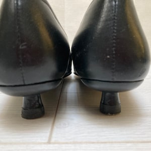 May include: A pair of black leather heeled shoes with a pointed toe. The shoes have a low heel and a simple design.