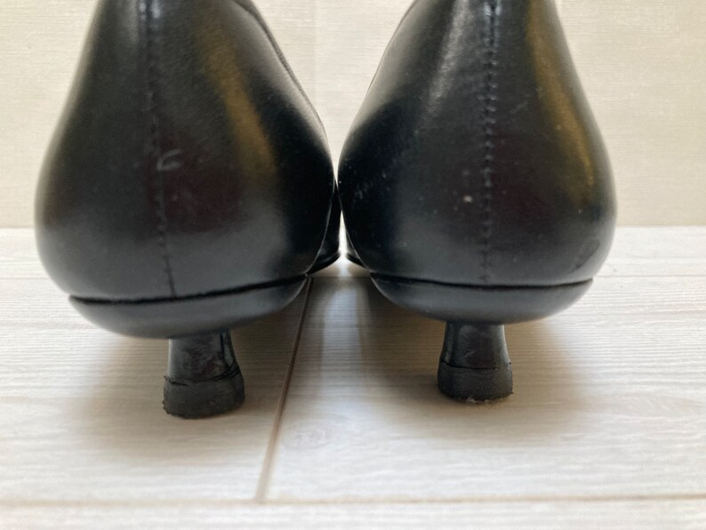 May include: A pair of black leather heeled shoes with a pointed toe. The shoes have a low heel and a simple design.