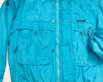 May include: A turquoise Descente ski jacket with a high collar, multiple pockets, and a zip-up front. The jacket has a small logo patch and snap closures. The jacket is made of a shiny, water-resistant material.
