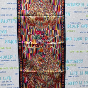 May include: A colorful silk scarf with a floral pattern and a repeating phrase "Give the best of yourself" on a white background.