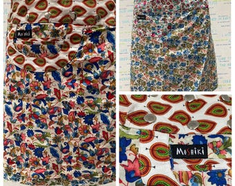 Puede incluir: Una falda blanca con un estampado floral colorido. La falda tiene un bolsillo en la parte delantera con la palabra "Moshiki" escrita en él. La falda tiene una cintura blanca con botones plateados.