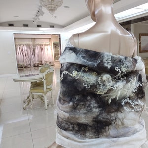 May include: A white and gray wool shawl with a textured, abstract design. The shawl is draped over a mannequin.