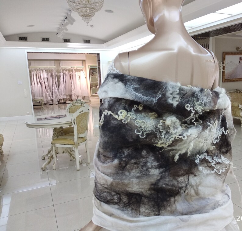 May include: A white and gray wool shawl with a textured, abstract design. The shawl is draped over a mannequin.