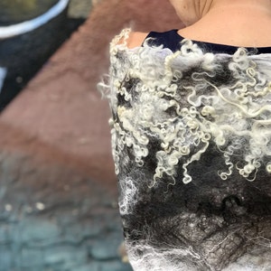 May include: A white and black wool shawl with a textured, curly design. The shawl is draped over a person's shoulders.