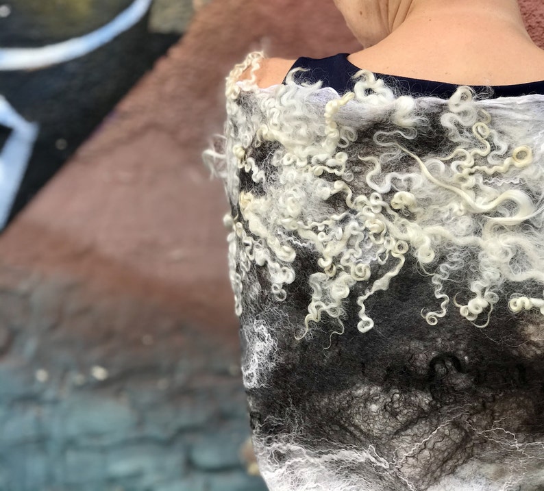 May include: A white and black wool shawl with a textured, curly design. The shawl is draped over a person's shoulders.