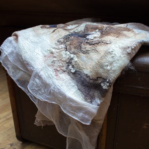 May include: A white and brown wool shawl with a delicate, lacy texture. The shawl is draped over a wooden chest.