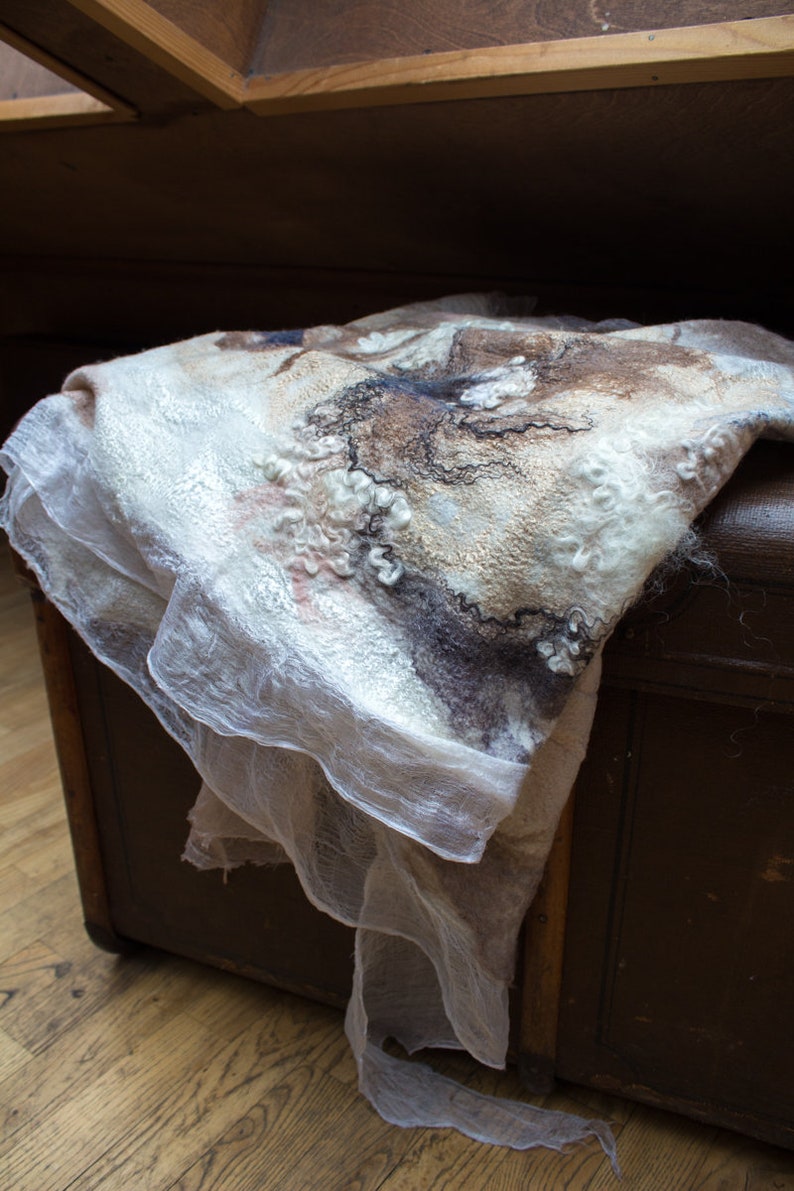 May include: A white and brown wool shawl with a delicate, lacy texture. The shawl is draped over a wooden chest.