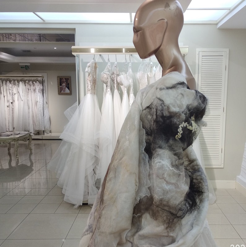 May include: A white wedding dress with a long, flowing skirt and a fitted bodice. The dress is made of a soft, flowing fabric and has a delicate lace trim. The dress is displayed on a mannequin in a bridal shop.
