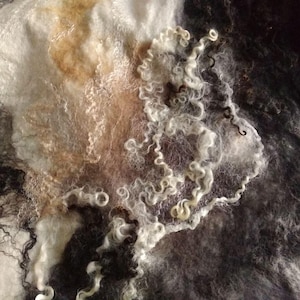 May include: A close-up of a white, brown, and black felted fabric with a swirling pattern. The fabric is soft and textured, and the colors are muted and subtle.
