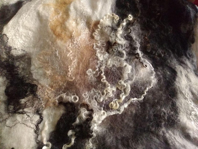 May include: A close-up of a white, brown, and black felted fabric with a swirling pattern. The fabric is soft and textured, and the colors are muted and subtle.