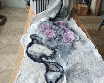 May include: A white wool shawl with black and gray abstract designs and pink flowers. The shawl is draped over a wooden surface.