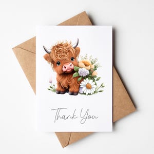 May include: A white card featuring a watercolour illustration of a Highland cow calf with flowers. The card reads "Thank You" in a handwritten font. A brown envelope is visible behind the card.