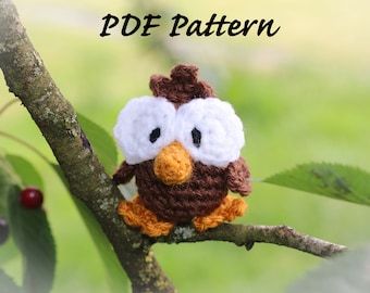 May include: A brown and white crocheted owl with large white eyes and an orange beak, perched on a branch.