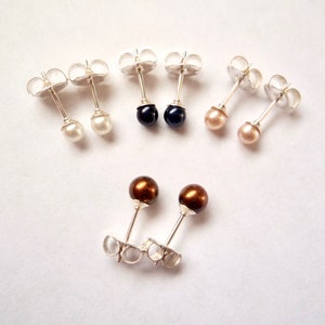 May include: A set of six pearl stud earrings in various colors, including white, black, brown, and pink. The earrings are silver and have a simple design.