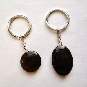 May include: Two black gemstone keychains with silver key rings and chains. One keychain has a round gemstone and the other has an oval gemstone.