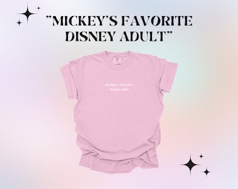 May include: A pink t-shirt with the text "mickey's favorite disney adult" printed on the front.