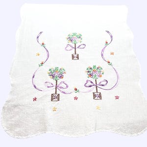 May include: White, scalloped-edge towel with embroidered floral designs. Three floral arrangements with purple bows and ribbons are centered on the towel. Additional embroidered flowers and accents in red, yellow, and green complete the design.