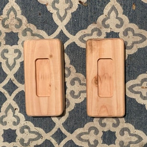 May include: Two wooden rectangular blocks with a rectangular cutout in the center. The blocks are light brown and have a smooth finish.