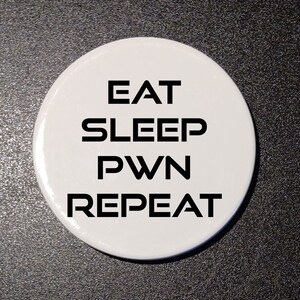May include: Four white round buttons with black text that reads "EAT SLEEP PWN REPEAT".
