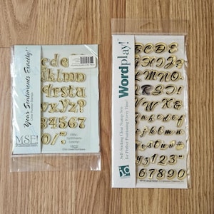 May include: Two sets of clear rubber stamps in plastic packaging. The left set, labeled Your Sentiments Exactly!, contains lowercase letters and numbers. The right set, labeled Wordplay!, features uppercase and lowercase letters and numbers.