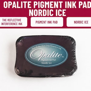 May include: A rectangular Opalite pigment ink pad in the color Nordic Ice. The product is encased in clear plastic wrap and features a central oval label with the text The Reflective Interference Ink, Opalite, Pigment Ink Pad, and Nordic Ice.