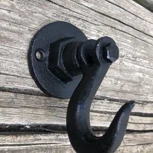 May include: Black metal hook with a round base and a hexagonal nut design. The hook is mounted on a wooden surface.