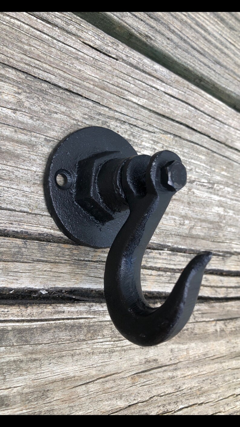 May include: Black metal hook with a round base and a hexagonal nut design. The hook is mounted on a wooden surface.