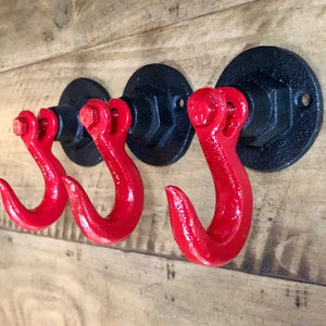 May include: Three black metal hooks with red metal hooks attached to the wall. The hooks are mounted on a wooden surface.