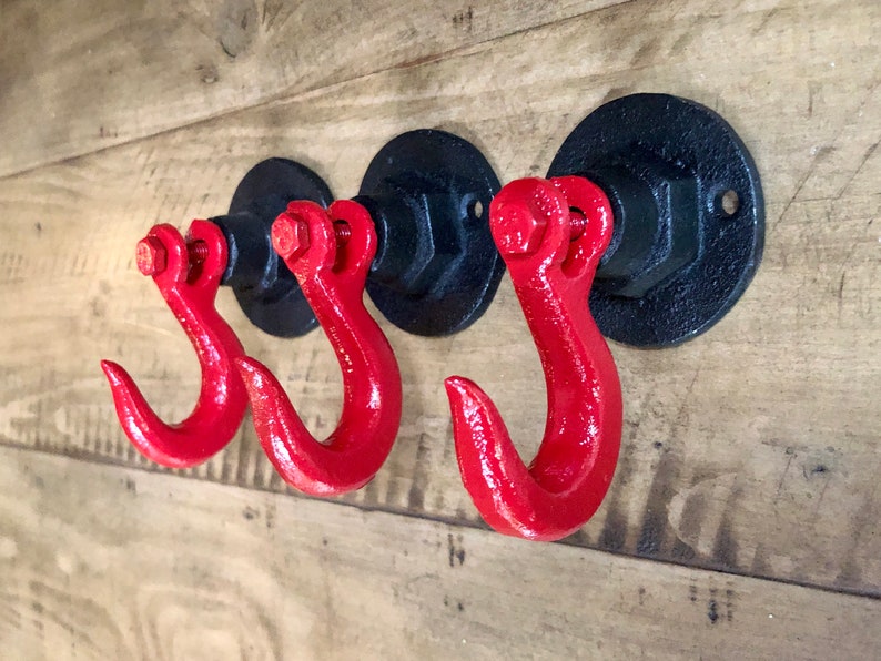 May include: Three black metal hooks with red metal hooks attached to the wall. The hooks are mounted on a wooden surface.