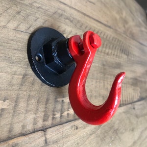 May include: A red metal hook with a black metal base. The hook is attached to a wall with a screw.