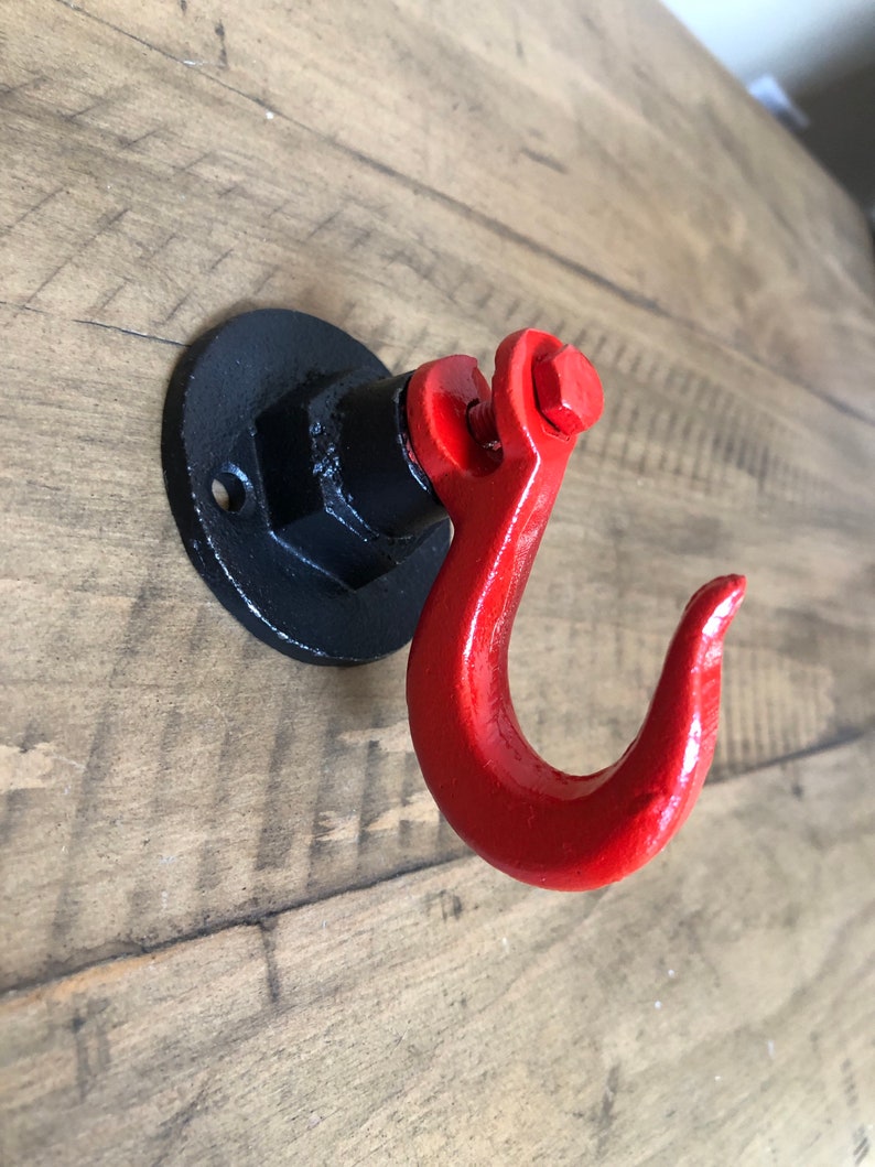 May include: A red metal hook with a black metal base. The hook is attached to a wall with a screw.