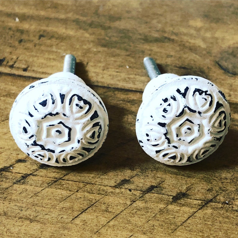 May include: Two white ceramic cabinet knobs with a black floral design. The knobs have a distressed finish and a simple screw-on design.