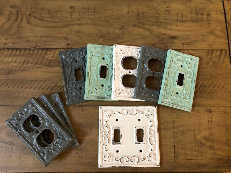 May include: Set of decorative light switch and outlet covers in various colors, including white, gray, and teal. The covers feature an ornate, embossed design.