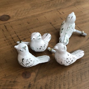 May include: Four white bird-shaped cabinet knobs with distressed paint and a rustic finish. Each knob has a metal screw for attaching to a drawer or cabinet door.