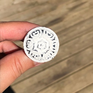 May include: White round knob with a black floral design.