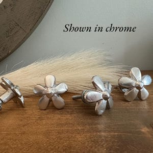 May include: Four silver flower-shaped cabinet knobs with a screw attachment. Shown in chrome.