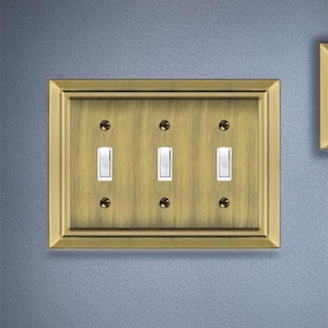 May include: A brass wall plate with three toggle switches. The plate has a decorative border and a brushed finish.