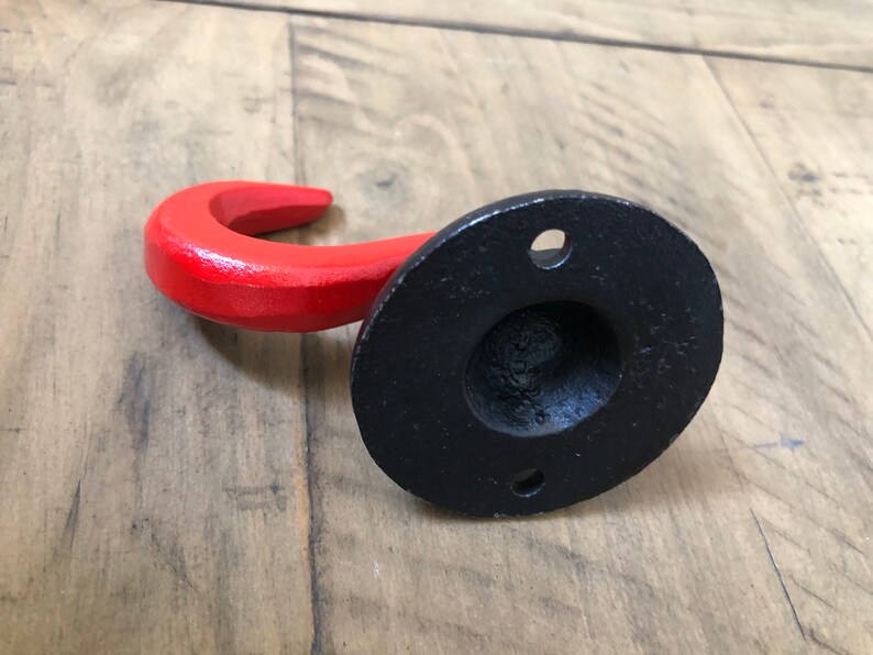 May include: A red metal hook with a black metal base. The hook is curved and has a smooth finish. The base has a round shape and a hole in the center for mounting.