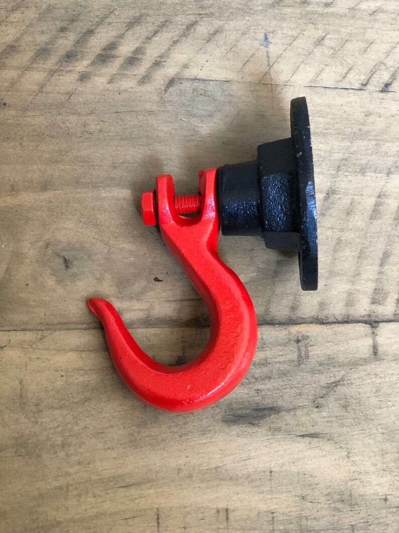 May include: A red metal hook with a black metal base. The hook is attached to the base with a screw. The hook is designed to be mounted on a wall.