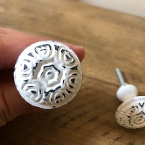 May include: White ceramic cabinet knob with a black floral design. The knob has a raised, textured surface.