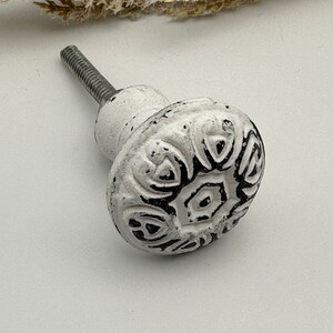 May include: White ceramic cabinet knob with a black floral design. The knob has a metal screw.