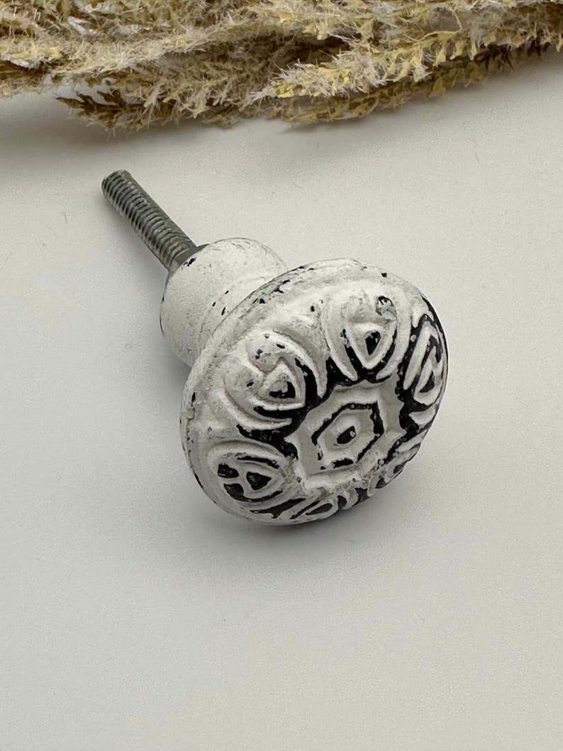 May include: White ceramic cabinet knob with a black floral design. The knob has a metal screw.