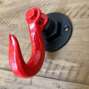 May include: A red metal hook with a black metal base. The hook is attached to a wall with a screw.