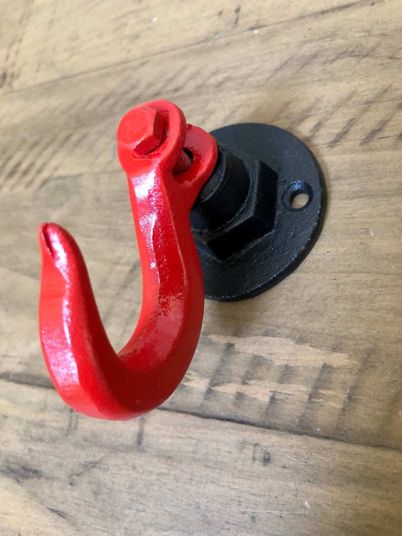 May include: A red metal hook with a black metal base. The hook is attached to a wall with a screw.